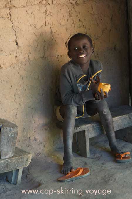 Jeune enfant fils de pêcheur, assis à la porte de sa case en terre. Sourire du Sénégal. Le bonheur est beau et apaisant.